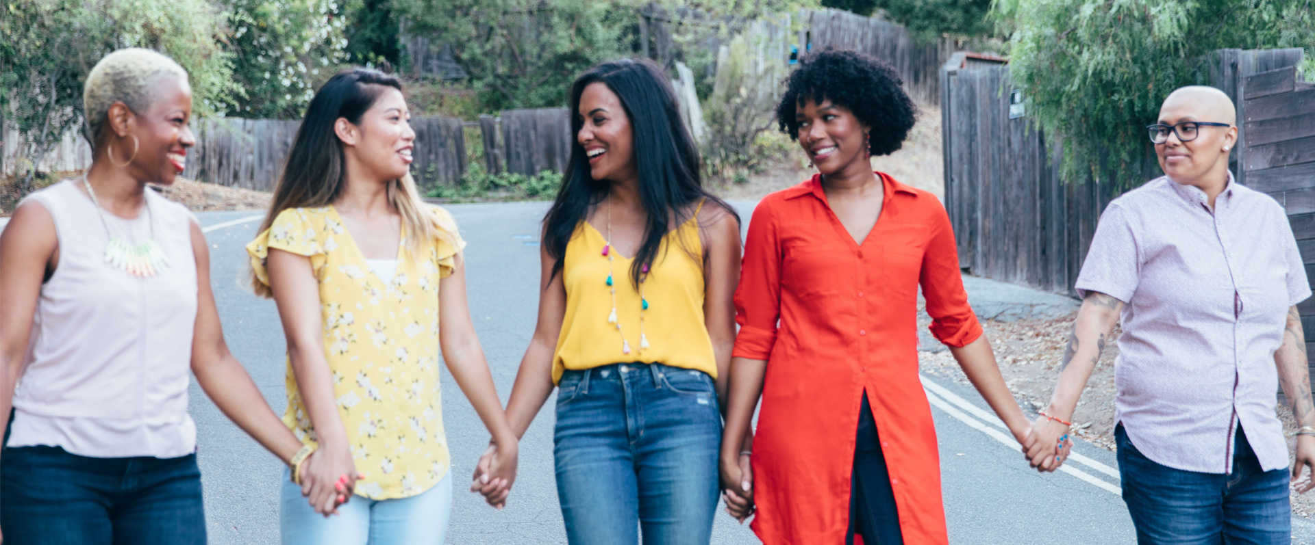 Five women of diverse ethnicities smiling and holding hands while walking outdoors on a road after a counseling session in Sherman Oaks.