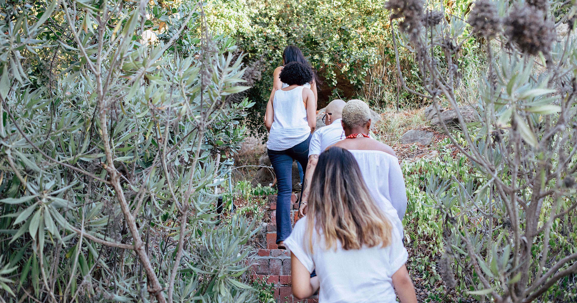Three people ascending a brick staircase outdoors in Sherman Oaks, surrounded by greenery.