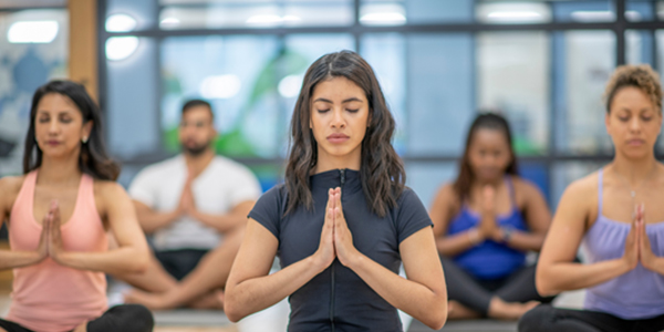 Group of people practicing yoga as therapy with focus on a woman in the foreground in a meditation pose.