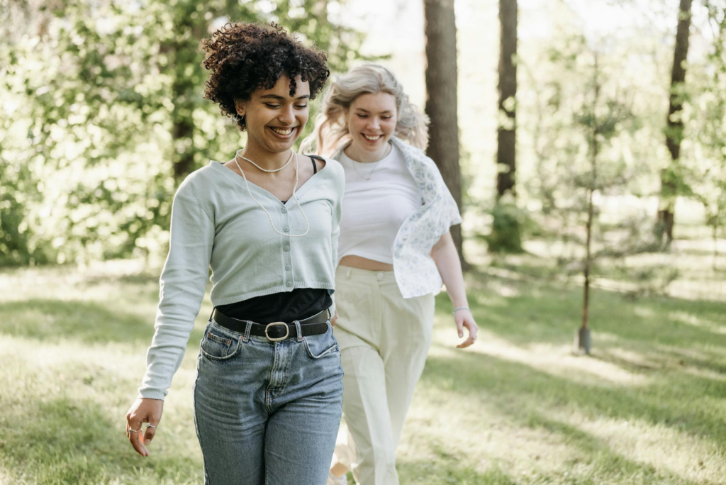 Two women of color walking and laughing together in a sunny park.